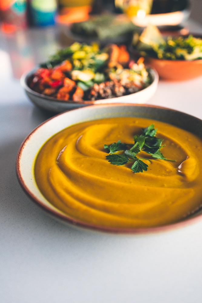 Bowl of golden sweet potato soup next to a grain bowl and burritos